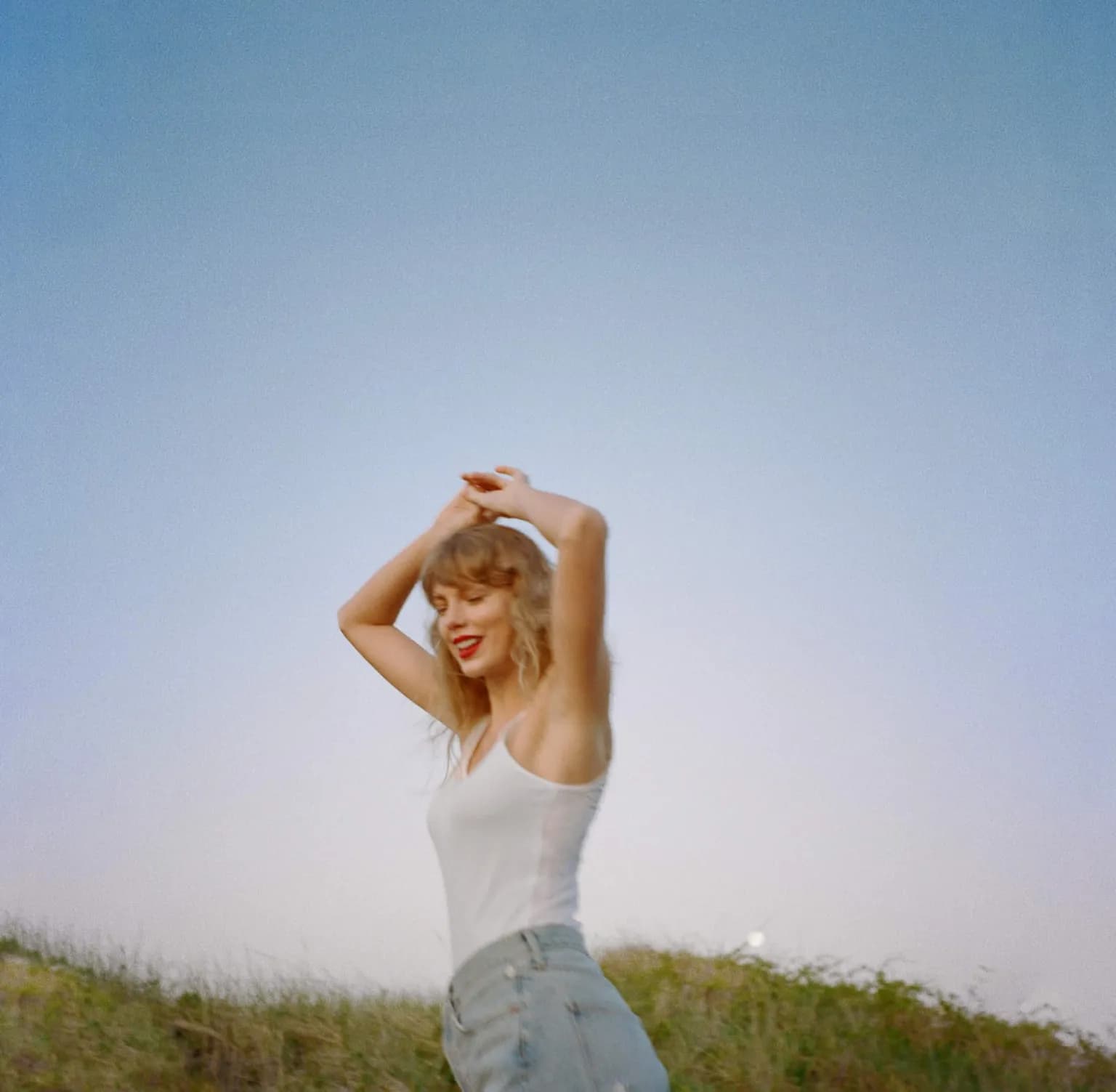 Taylor Swift smiling with her arms raised against a blue sky.