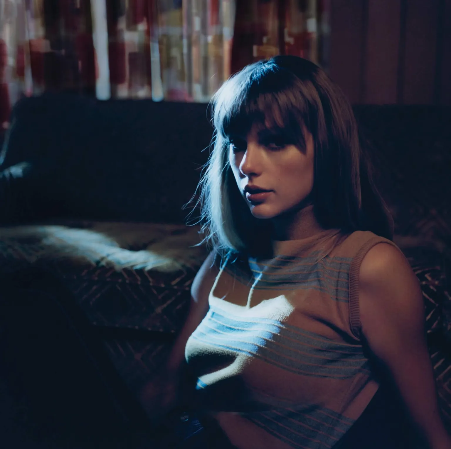 Taylor Swift seated in a striped top under blue light.